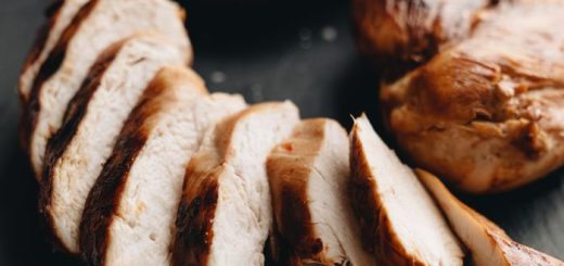 Close-up of grilled chicken breasts sliced on slate with tomato garnish.
