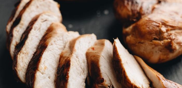 Close-up of grilled chicken breasts sliced on slate with tomato garnish.