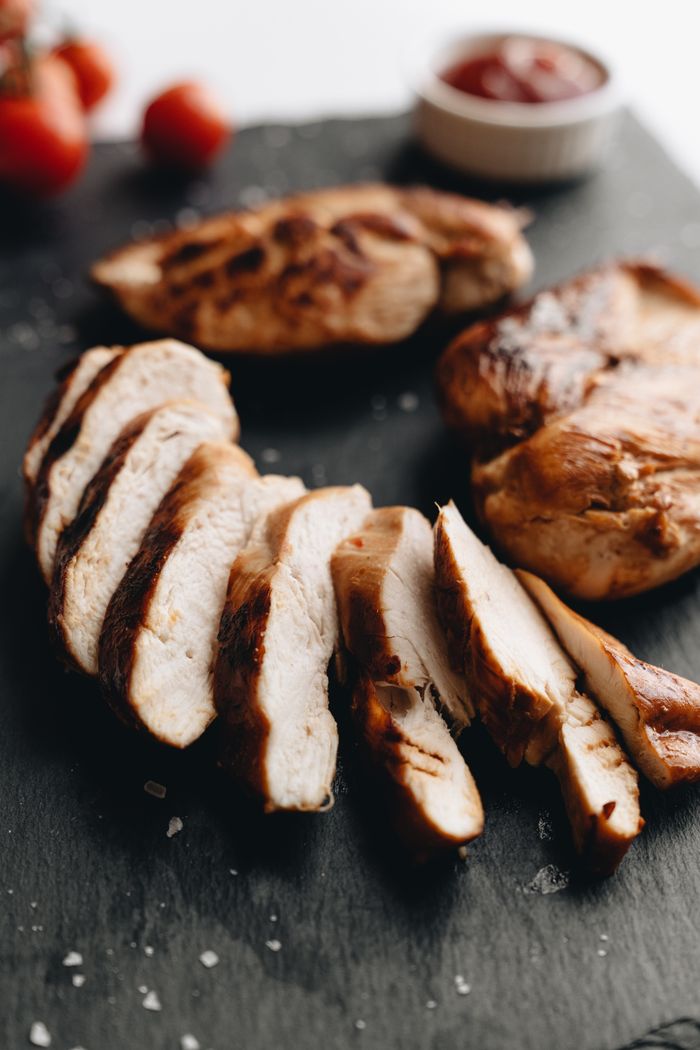 Close-up of grilled chicken breasts sliced on slate with tomato garnish.
